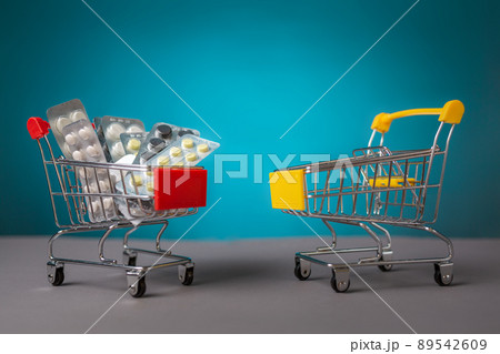 Two small carts, empty and filled with pills, stand on a blue background. Copy space. Concept of coronavirus, business and pharmaceuticals 89542609