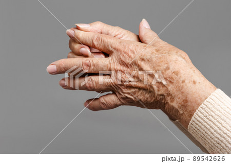 A senior woman massages her fingers, experiencing pain in the joints. Gray background, hands close-up. The concept of rheumatism and arthritis 89542626