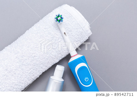 Electric toothbrush, toothpaste, and white towel on a gray background. Flat lay. The concept of electronic devices for personal hygiene Electric toothbrush, toothpaste, and white towel on a gray background. Flat lay. The concept of electronic devices for personal hygiene 89542711