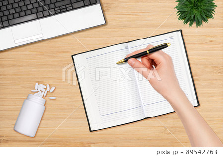 A woman's hand writes with a pen in a notebook. Next to it is a jar with scattered pills. Flat lay. The concept of treatment and planning A woman's hand writes with a pen in a notebook. Next to it is a jar with scattered pills. Flat lay. The concept of treatment and planning 89542763