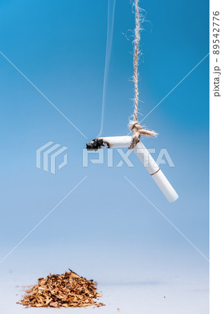 World Tobacco Control Day. Smoking cigarette hangs over a pile of tobacco on a blue background. Copy space. Vertical. The concept of nicotine addiction World Tobacco Control Day. Smoking cigarette hangs over a pile of tobacco on a blue background. Copy space. Vertical. The concept of nicotine addiction 89542776