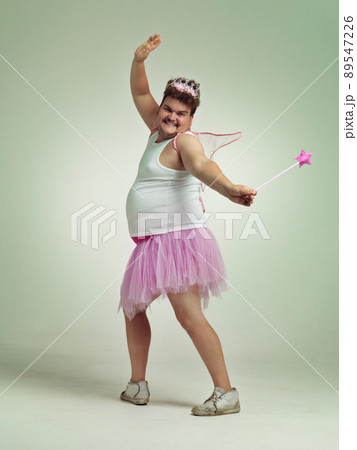 Magic wands are fun. An overweight man comically dressed-up in a pink fairy costume. 89547226