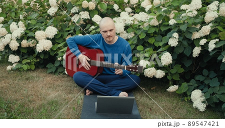 Man in with an acoustic guitar is sitting in a park in nature and is streaming online podcast using gadgets. The concept of travel, hiking, internet streams, hobbies and remote work Man in with an acoustic guitar is sitting in a park in nature and is streaming online podcast using gadgets. The concept of travel, hiking, internet streams, hobbies and remote work 89547421