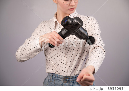 Caucasian business woman massaging her biceps with a percussion massager. 89550954
