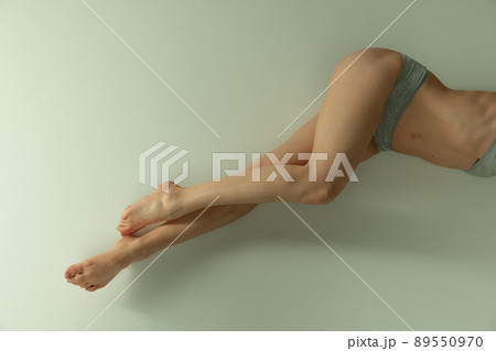 Beautiful slender female legs in gray underwear, laying over grey background. Anti-cellulite care 89550970