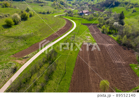 Aerial view of village road passing near an agricultural field Aerial view of village road passing near an agricultural field 89552140