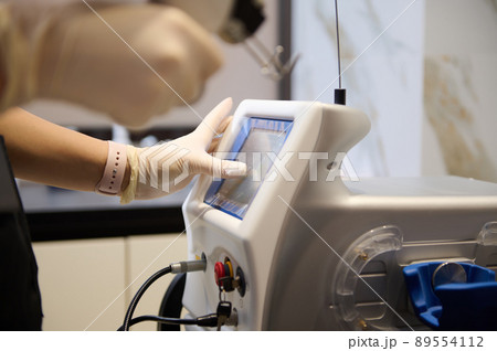 Close-up of beauty therapist hands holding laser resurfacing machine, pointing with finger at the monitor screen, adjusting programs on hardware beauty apparatus Close-up of beauty therapist hands holding laser resurfacing machine, pointing with finger at the monitor screen, adjusting programs on hardware beauty apparatus 89554112