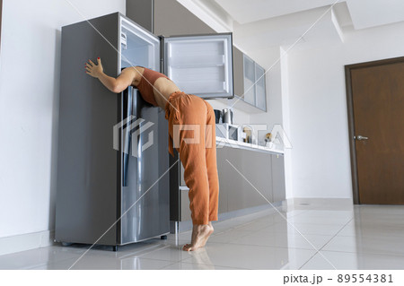 On a hot day, the girl cools with his head in the refrigerator. Broken air conditioner On a hot day, the girl cools with his head in the refrigerator. Broken air conditioner 89554381