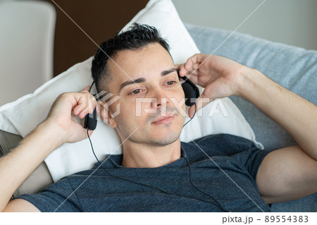the guy enjoys the music while lying on the couch with headphones. Relaxation with music 89554383