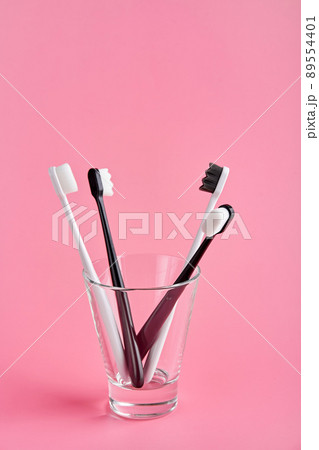 Fashionable toothbrush with soft bristles. Popular toothbrushes. Hygiene trends. Kit of toothbrushes in glass on pink background Fashionable toothbrush with soft bristles. Popular toothbrushes. Hygiene trends. Kit of toothbrushes in glass on pink background 89554401
