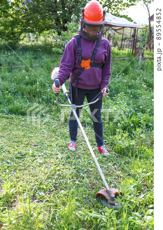 Woman farmer mows the grass in the backyard using string trimmer Woman farmer mows the grass in the backyard using string trimmer 89554852