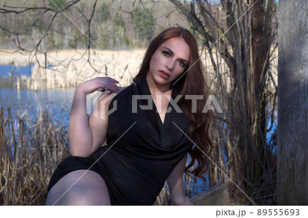 young woman in black dress sitting in the forest near water pond in sunshine young woman in black dress sitting in the forest near water pond in sunshine 89555693