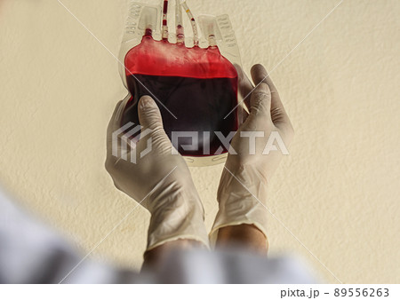 Woman holding blood for transfusion on beige background, closeup. Donation concept 89556263