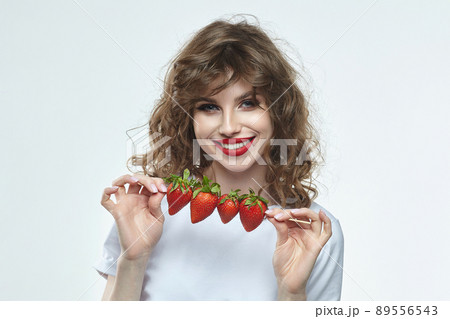 attractive girl is holding a skewer on which strawberries are strung. 89556543