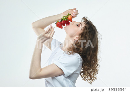 attractive girl is holding a skewer on which strawberries are strung. 89556544