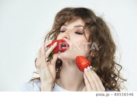 attractive girl holds two strawberries in front of her face. 89556546