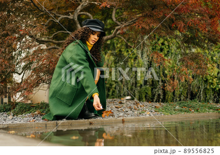 At the backwater in the park crouched girl and reaches for the water hand which holds a red sheet autumn 89556825