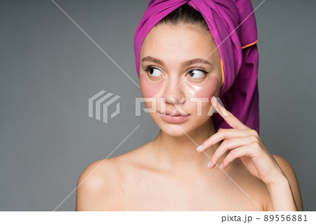 close-up. A girl with nude shoulders with a towel on her head conducts spa procedures by sticking patches under her eyes 89556881