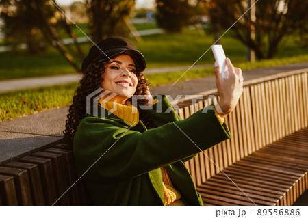 Sitting on a bench in the park and flaunting looks at himself in the phone screen and makes selfies a beautiful girl 89556886
