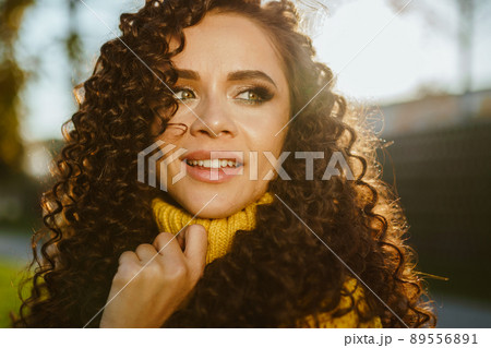 turning over her shoulder with a smile looking into the distance with green eyes looking curly brunette close-up 89556891