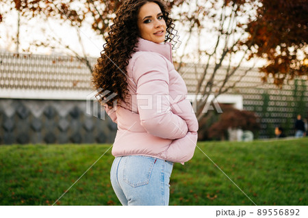 The curly beautiful brunette in a down jacket stands back in half way to the camera in slinky jeans beautifully accentuating her hips 89556892