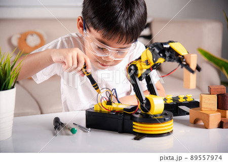 Happy Asian little kid boy using screwdriver to fixes screws robotic machine arm in home workshop 89557974