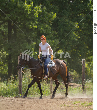 A redhead woman in white t-shirt and glasses riding a horse in nature. A redhead woman in white t-shirt and glasses riding a horse in nature. 89561629