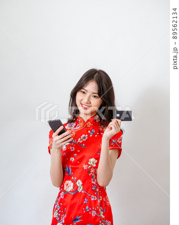Portrait of a young asian woman wearing traditional cheongsam qipao dress using smartphone with credit card on white background. Portrait of a young asian woman wearing traditional cheongsam qipao dress using smartphone with credit card on white background. 89562134