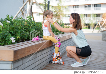 Caucasian woman helping her daughter put on roller skates. 89565535