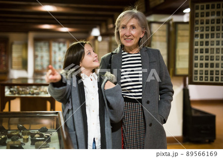 Aged female tutor with preteen girl exploring showpieces in museum Aged female tutor with preteen girl exploring showpieces in museum 89566169