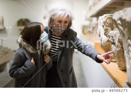 Preteen girl in protective mask visiting museum of ancient sculptures with grandmother Preteen girl in protective mask visiting museum of ancient sculptures with grandmother 89566275