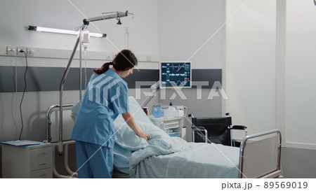 Medical assistant preparing hospital ward bed for patient at facility. Woman working as nurse getting intensive care room ready for healthcare treatment and recovery of sick person Medical assistant preparing hospital ward bed for patient at facility. Woman working as nurse getting intensive care room ready for healthcare treatment and recovery of sick person 89569019