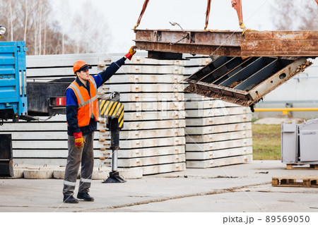 Slinger in helmet and vest controls unloading of metal structures on construction site. White 89569050