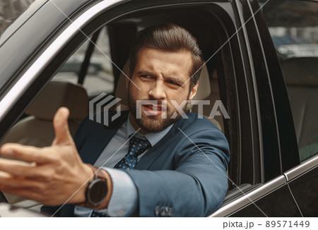 Confused male in suit gesturing from car Confused male in suit gesturing from car 89571449