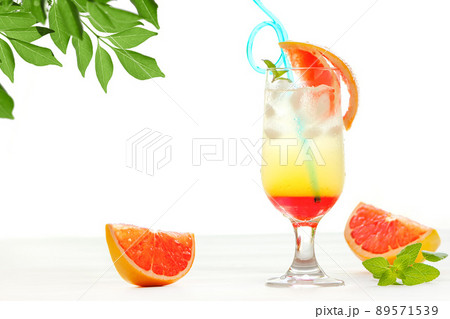 海を背景に2層になったオレンジとパイナップルのトロピカルジュースがテーブルの上に置かれている 89571539