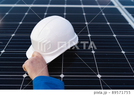 Hand of the engineer takes the helmet that lies on the solar panel. Alternative energy concept. 89571755