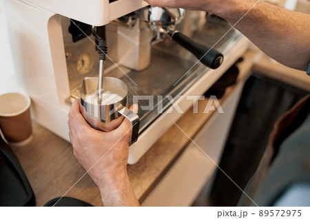 Close up of barista hands heating up milk in pitcher with steam 89572975