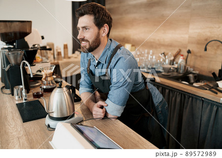 Handsome smiling barista waiting for clients in modern loft cafe Handsome smiling barista waiting for clients in modern loft cafe 89572989
