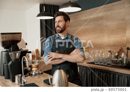 Handsome young coffeeshop owner standing behind the counter and looks away 89573001