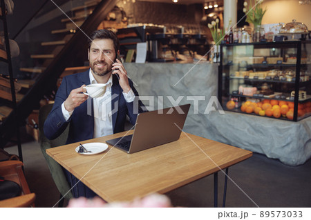 Attractive Caucasian businessman talking on mobile phone and drinking coffee. Business. Attractive Caucasian businessman talking on mobile phone and drinking coffee. Business. 89573033