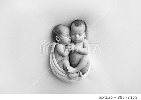 Tiny newborn twins boys in white cocoons on a white background. A newborn twin sleeps next to his brother. Newborn two twins boys hugging each other.Professional black and white studio photography. Tiny newborn twins boys in white cocoons on a white background. A newborn twin sleeps next to his brother. Newborn two twins boys hugging each other.Professional black and white studio photography. 89573155