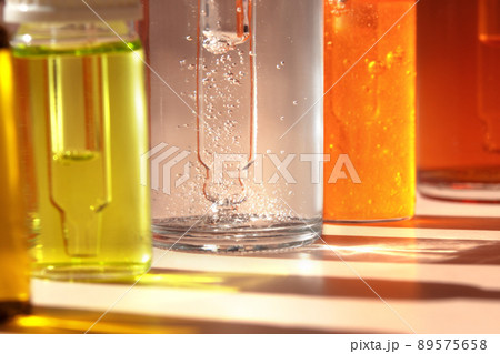 Different cosmetic glass bottles standing in a row on light background. Macro. Soft focus. Abstract colorful pattern in the sunlight. Red, green and yellow shades. Front view with copy space Different cosmetic glass bottles standing in a row on light background. Macro. Soft focus. Abstract colorful pattern in the sunlight. Red, green and yellow shades. Front view with copy space 89575658