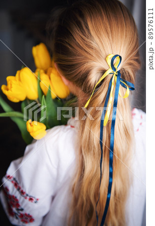 A little Ukrainian girl in traditional clothes holds a yellow tulips in her hands 89576111