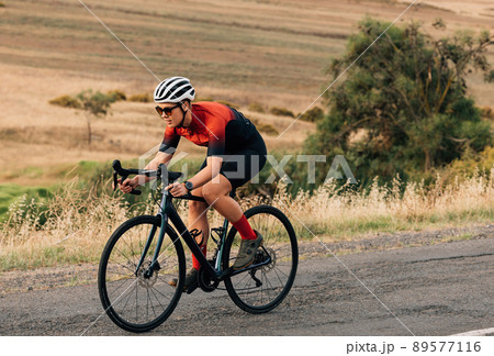 Woman riding a bicycle on empty road. Sportswoman in fitnesswear practicing on pro bike. 89577116