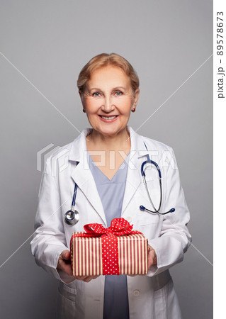 Smiling medical physician doctor holding red gift box on grey background 89578673