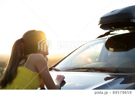 Yong happy woman standing near her car enjoying sunset view of summer nature. Travel and getaway concept. Yong happy woman standing near her car enjoying sunset view of summer nature. Travel and getaway concept. 89579659