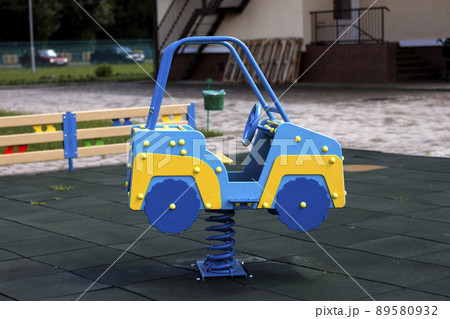 New modern plastic bright colorful blue and yellow big toy car on spring on nursery playground with soft rubber flooring on bright sunny summer day. Perfect place for children activities outdoors. New modern plastic bright colorful blue and yellow big toy car on spring on nursery playground with soft rubber flooring on bright sunny summer day. Perfect place for children activities outdoors. 89580932