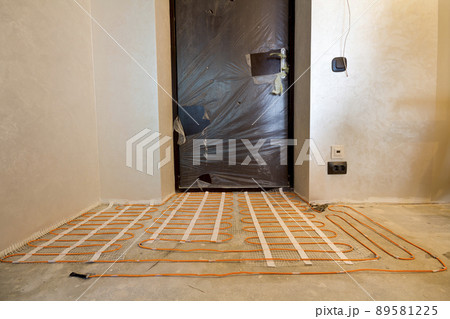 Heating red electrical cable wire system installed on cement floor in small new unfinished room with plastered walls. Renovation and construction, modern technology, comfortable warm home concept. 89581225