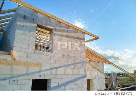 Aerial view of unfinished frame of private house with aerated lightweight concrete walls and wooden roof frame under construction. Aerial view of unfinished frame of private house with aerated lightweight concrete walls and wooden roof frame under construction. 89582779
