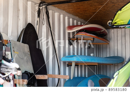 Interior of windsurf boards storage room in old rusty metal shipping container box with racks on wall. Used shabby surfboards rental and warehouse. Watersport equipment gear tools 89583180